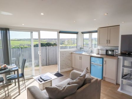 A kitchen and living area with a blue fridge sofa and glass doors opening to a patio at Gannel Hideaway in Newquay