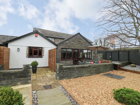 A stone and white exterior house with a gravel yard a patio with outdoor furniture and an umbrella at Dant Y Llew in Bow Street Wales