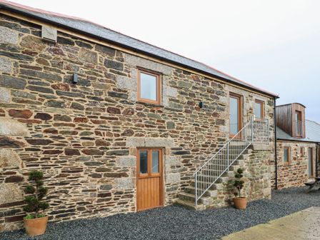 Stone building with wooden doors and windows with an external metal staircase and potted plants outside at Pol View in Gunwalloe near Helston