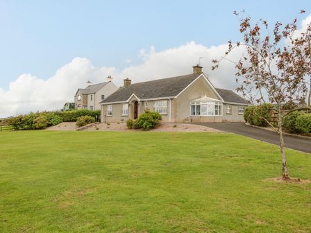 A bungalow with a driveway and a small tree on a lawn at Braeside Farm House Cloughmills