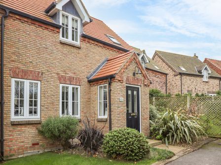 A front view of a brick house with a black door and several windows surrounded by shrubs at STAKS Cottage The Bay Holiday Village near Filey
