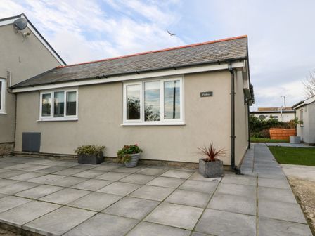 A single-story building with three windows and three potted plants on a tiled patio at Cedars in Holyhead