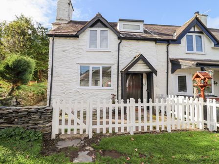 A white stone cottage with a black door and white picket fence in front at 1 Hendom in Llangollen