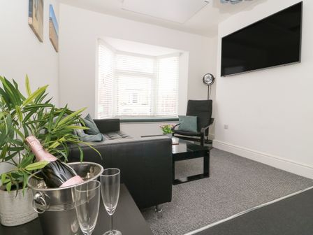 A living room with a black sofa black armchair coffee table and a wall-mounted television at Wave and Sea in Bridlington