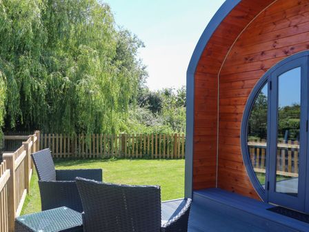 A garden area with wicker chairs and a wooden pod with round windows at Willow Pod in Arundel West Sussex