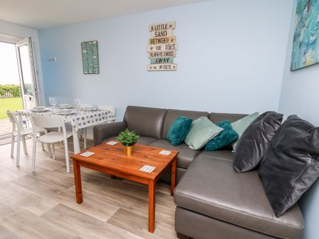 A living area with a brown sofa with cushions and a wooden coffee table next to a dining table set with plates and glasses at Cwtsh Cragen in New Quay