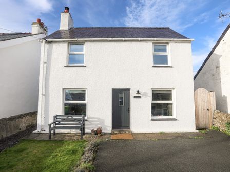 A white two-story house with a dark grey door a bench and a small lawn at Disgwylfa in Moelfre