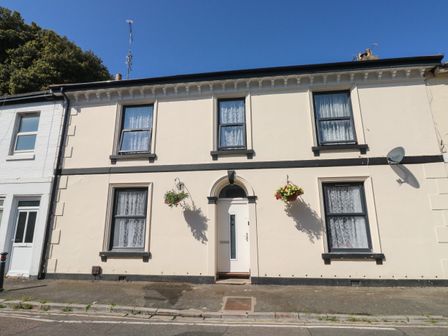 A cream colored two story house with black window frames hanging flower baskets and a white door at 11 Magdalene Road in Torquay