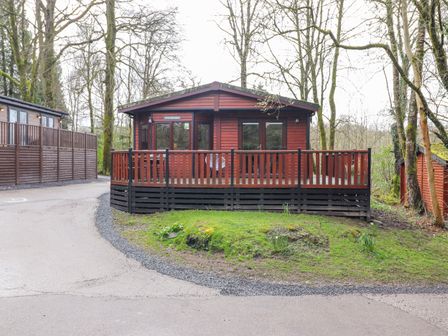 A wooden cabin with a fenced porch surrounded by trees at Alfresco Lodge in Skiptory Howe 37B White Cross Bay near Windermere
