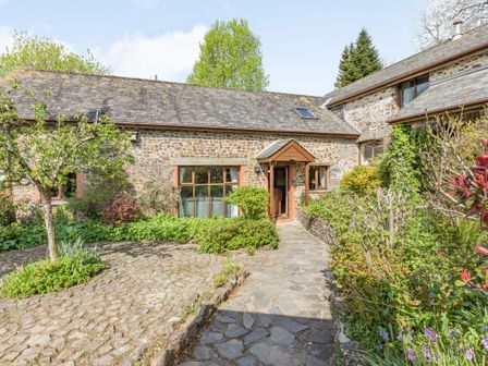 A stone house with a tiled roof and garden path surrounded by greenery at Hazel Barn in North Molton
