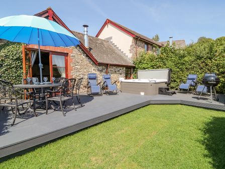 An outdoor patio with a dining table and umbrella lounge chairs hot tub and barbecue grill at Oak Cottage in North Molton