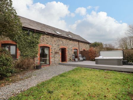 Exterior of stone house with gravel path garden chairs and hot tub on wooden deck at The Hawthorns in North Molton