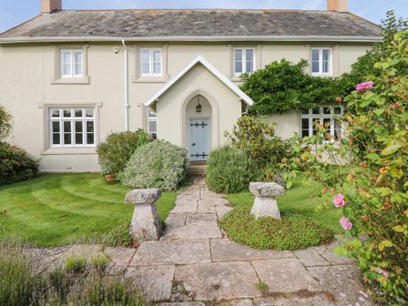 The front exterior of a house with a stone pathway leading to a blue front door surrounded by bushes and flowers at Crablake Farmhouse in Exminster