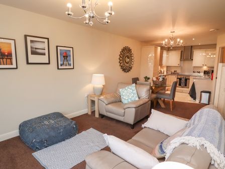A living room with sofas cushions a lamp wall art and an open kitchen with dining table and chairs at Explorers Rest Whitby