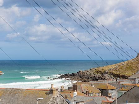 A coastal view with rooftops in the foreground rocky shoreline and ocean waves under a partly cloudy sky at Hepworth Apartment in St Ives