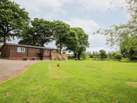 A wooden cabin with stairs and potted plants near a green lawn with small red flags and trees in the background at The Log Cabin in Newnham Bridge near Tenbury Wells