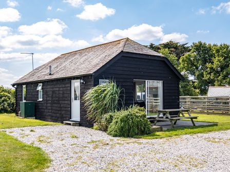 A black wooden cabin with a gravel driveway and picnic table on grass at Atlantic Lodge in Port Isaac