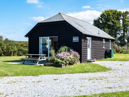 A small black wooden house with flowers and a picnic table outside at Harbour Lodge in Port Isaac