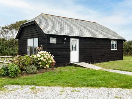 A small black wooden cabin with a white door and window a garden with flowers and a picnic table outside at Dolphin Lodge in Port Isaac