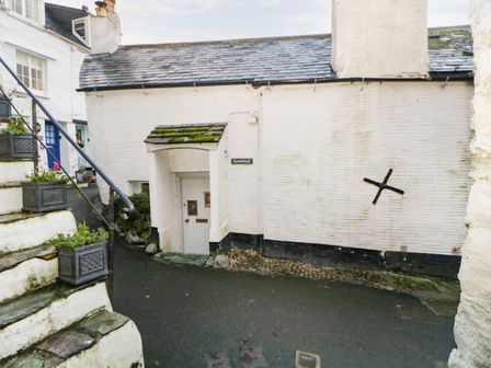 A white building with a small door under a mossy canopy and steps with flower pots at Spindrift in Polperro