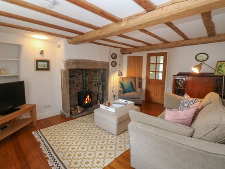 A living room with a fireplace a beige sofa and armchair a wooden cabinet and a television at Cross View Cottage in Alston