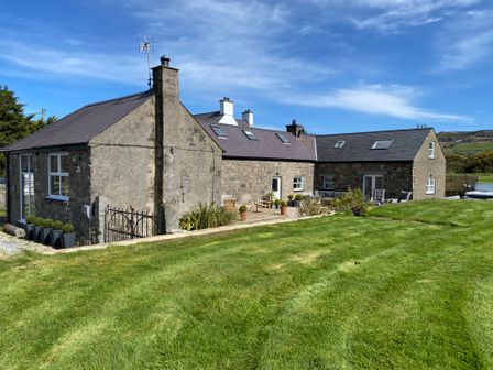 A stone farmhouse with a slate roof and outdoor seating on a grassy lawn at Farmhouse in Nefyn