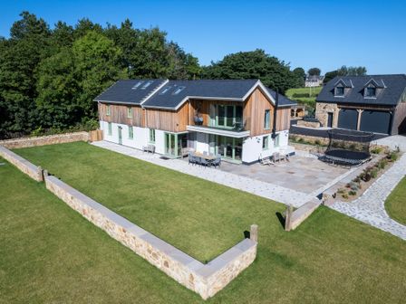 A modern two-story house with a wooden and white exterior a large lawn a stone wall a patio with outdoor furniture and a trampoline at Rynys in Llanddeiniolen near Llanrug