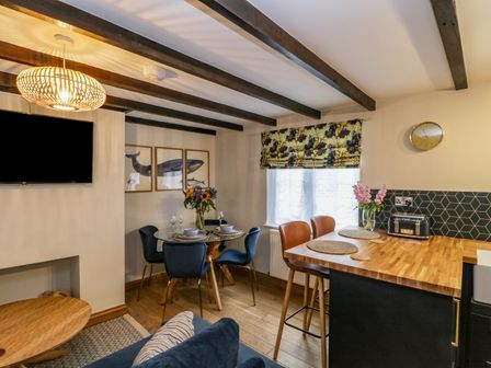Dining area with glass table and blue chairs next to kitchen island with wooden countertop and bar stools at April Cottage in Whitby