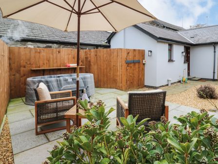 An outdoor patio area with a hot tub wooden chairs a table with an umbrella and a wooden fence at Llygad Y Dydd in Bow Street Wales