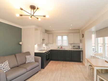 A kitchen area with dark and light cabinets a grey sofa with patterned cushions and a wooden dining table with chairs at Estuary Walk in Whitby