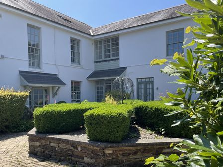 A garden with well-trimmed bushes and a building in the background at 2 The Manor House, Hillfield Village Dartmouth