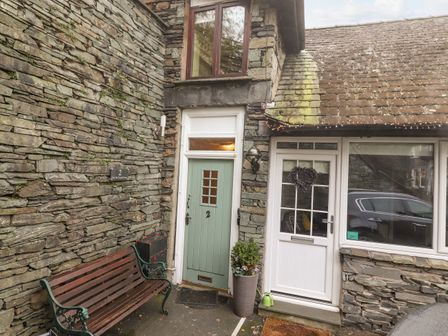 An exterior view of a stone house with a green door numbered 2 a white door with a wreath wooden bench and potted plants at 2 The Old Coach House Ambleside