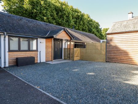 A house exterior with a gravel driveway wooden fence and trees at Clonmore in Bodmin