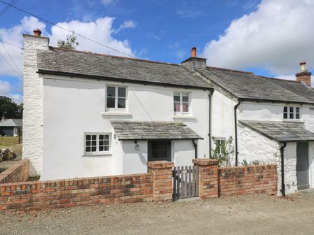 A white cottage with a tiled roof a brick wall and a wooden gate at Trelash Cottage in Trelash near Boscastle