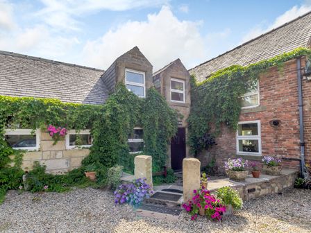 A stone house entrance with ivy on walls and flower pots on gravel at The Granary in Longhirst near Morpeth