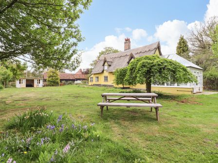 A garden with a picnic table flowers trees and a yellow thatched cottage at The Abbey Cottage in Windsor Green