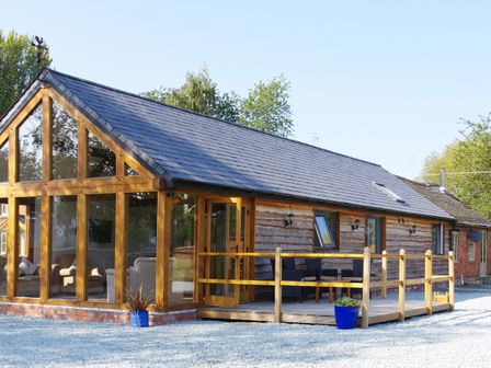 A wooden cabin with large glass windows and a small porch with chairs and tables at Haimwood Byetake in Llandrinio