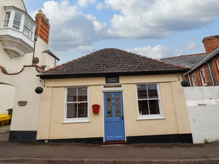 A small beige cottage with a blue front door and two windows on a street at Hardings cottage in Minehead