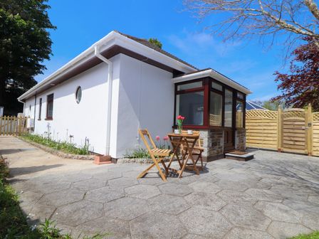 A small patio area with wooden table and chairs next to a white house with a glass porch at Swans Nest in Falmouth