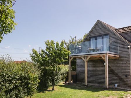 A wooden house with a glass balcony and outdoor furniture surrounded by trees and grass at Little Knaplock in Fiddington near Combwich Somerset