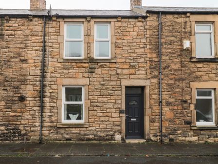 A stone brick house with a black front door and multiple windows at Coras House in Amble
