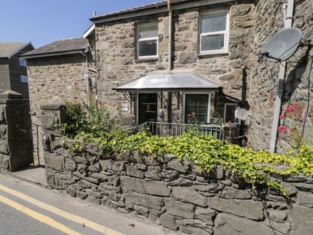 Stone building with two windows and two doors behind a stone wall with plants at 4A Victoria Place in Barmouth