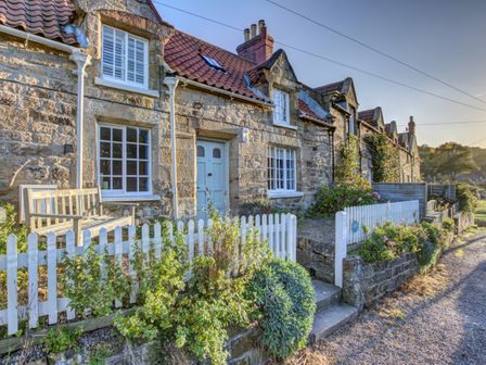 A row of stone cottages with white picket fences and gardens along a gravel path at Crab Cottage in Sandsend
