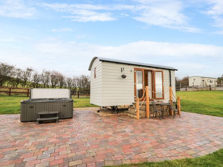 An outdoor patio with a small beige cabin hot tub and metal table with two chairs at Highland View in Rhayader