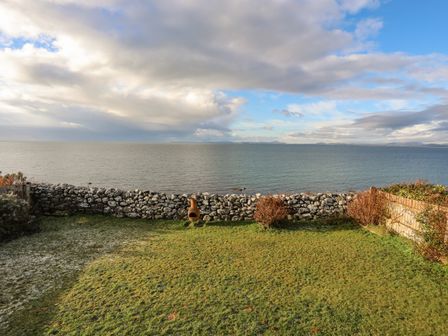 A grassy garden with a stone wall and ocean view at Bramble Bank in Llandanwg near Harlech