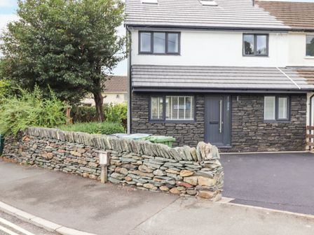 A house with a stone wall and driveway with green bins and trees nearby at Rydal Rock in Ambleside