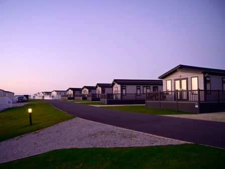 A row of modern static caravans along a paved road with grass and gravel at Rose View in Hendra Croft near Goonhavern