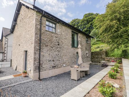 A stone exterior of a house with outdoor dining table and chairs and garden pathway at Bank Hurst Coach House in Ulverston