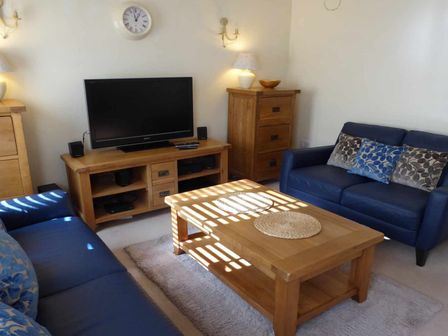 A living room with blue sofas a wooden coffee table a television on a wooden stand and wooden cabinets at House on the Green in Chipping Norton