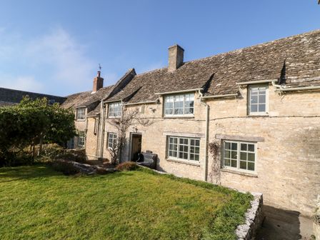 A stone cottage with multiple windows and a green lawn in front at Holly Cottage in Minster Lovell